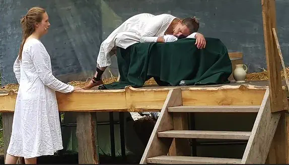 Scène uit de openluchtvoorstelling De Heks van Almen waarin twee vrouwen in witte kleding een emotioneel moment delen op het podium.