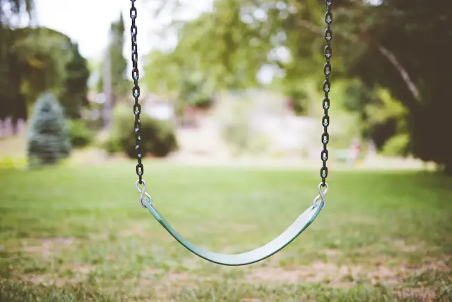 Lege schommel in de tuin als beeld voor het empty-nest syndroom Lege schommel in een tuin, zacht bewegend in de wind, als metafoor voor het empty-nest syndroom en het gemis van kinderen die uitvliegen