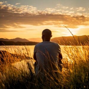 Deze foto toont een man in het gras, die uitkijkt over het water, om weer rustig te worden in zijn hoofd