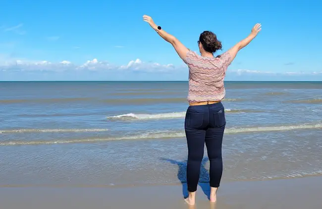Mieke Loor van Jouw Eigen Veerkracht staat met haar armen omhoog aan zee, symbool voor eindelijk weer ruimte en rust voelen