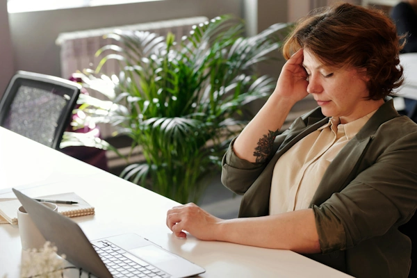 Vrouw met hoofdpijn zit achter laptop met handen in het haar door werkstress