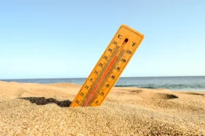 Thermometer in het zand op het strand met hoge temperatuur en zee op de achtergrond