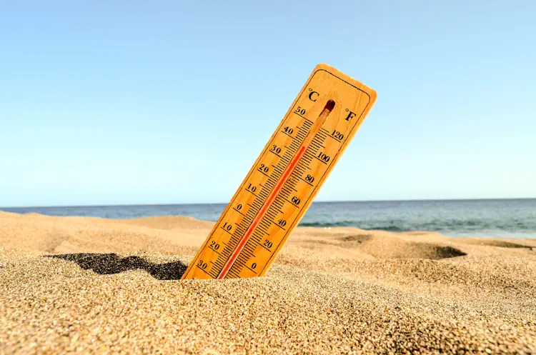 Thermometer in het zand op het strand met hoge temperatuur en zee op de achtergrond