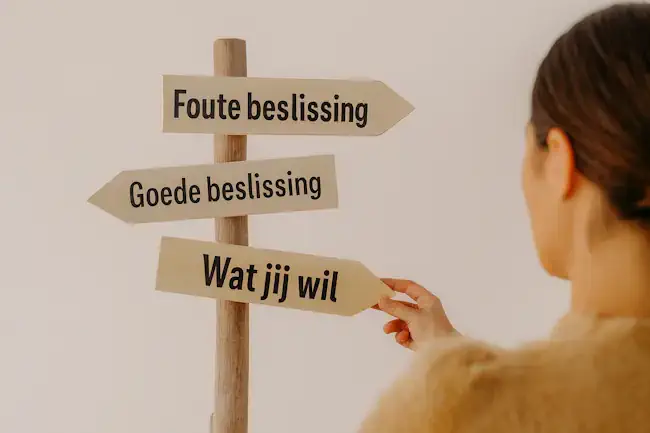 Houten wegwijzer met pijlen waarop staat foute beslissing, goede beslissing en wat jij wil, symbool voor eigen keuzes maken.