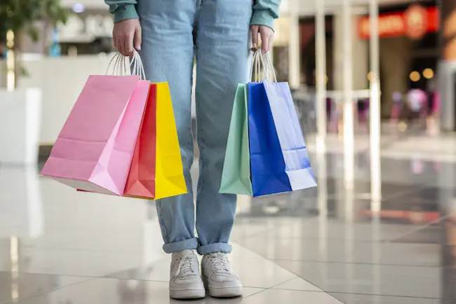 Persoon met gekleurde tassen na troostkopen in winkelcentrum – symbool voor emotieaankopen en onbewust shopgedrag