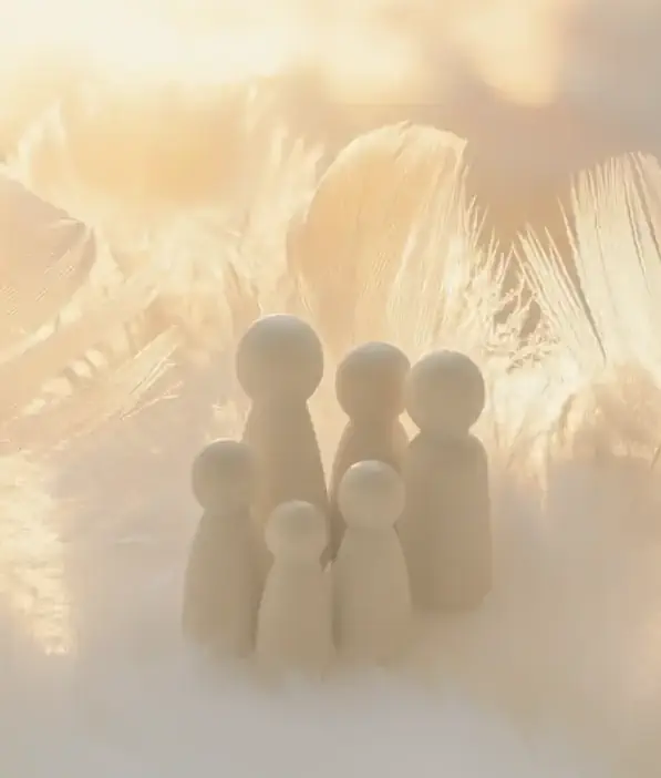 Houten figuurtjes tussen veren in warm licht, symbool voor systemisch werk en onderlinge verhoudingen