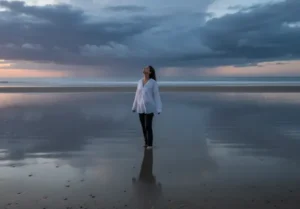 Vrouw staat alleen op het strand na een storm, symbool voor leven oppakken na jaren van onzekerheid en angst