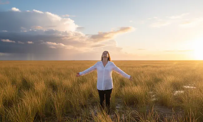 nieuw-begin-na-onzekerheid-ruimte-voelen-na-ziekte Vrouw staat met open armen in een veld bij zacht licht, symbool voor ruimte voelen en opnieuw leven na onzekerheid